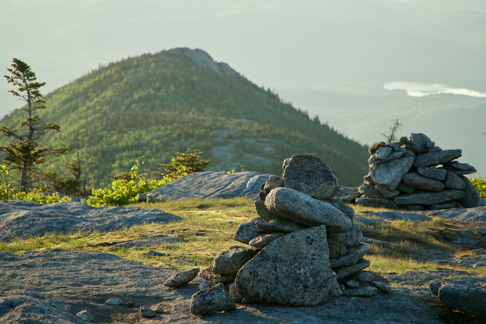 Two stone cairns on a rocky summit with a forested mountain behind
